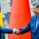 Lula e Xi Jinping apertam as mãos diante das bandeiras de Brasil e China