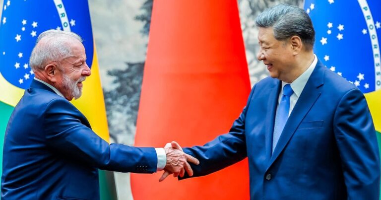 Lula e Xi Jinping apertam as mãos diante das bandeiras de Brasil e China