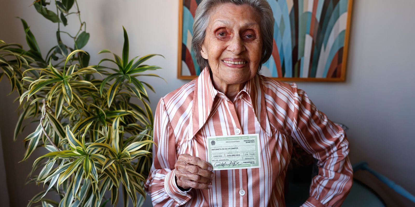 Eleitora idosa mostra o título de eleitor em sua residência