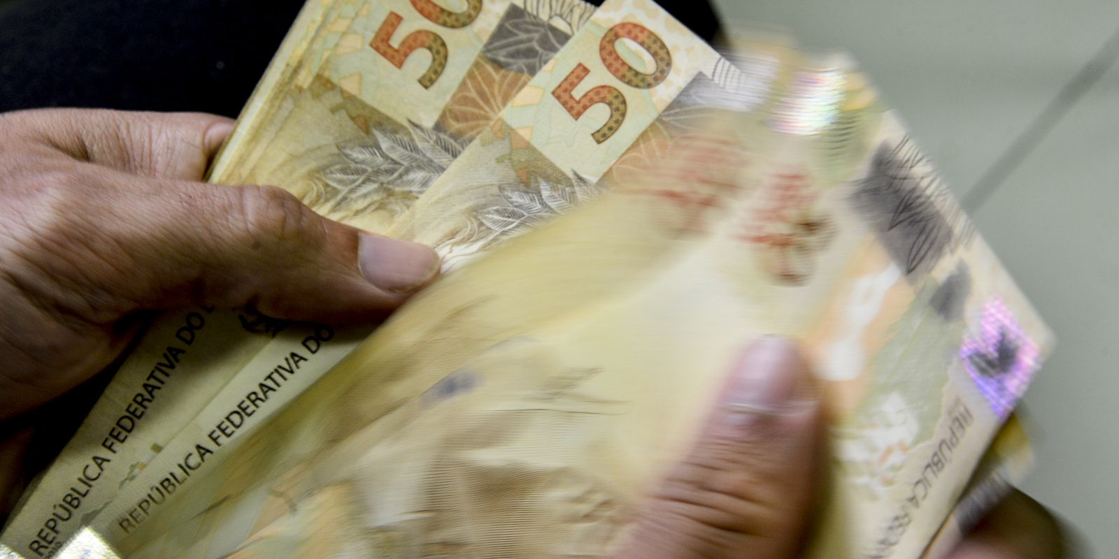 Pessoa manuseia notas de cinquenta reais