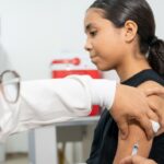 Adolescente recebe vacina aplicada por profissional de saúde