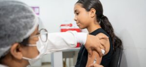Adolescente recebe vacina aplicada por profissional de saúde