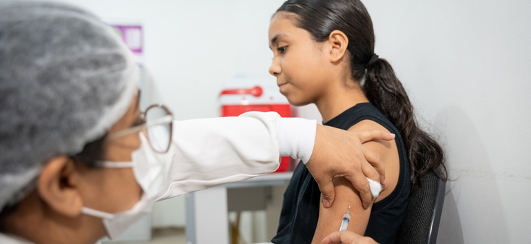Adolescente recebe vacina aplicada por profissional de saúde