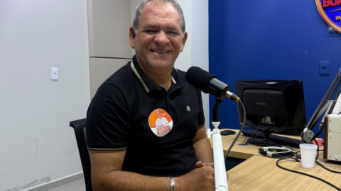 Mano Morais sentado diante de um microfone em estúdio de rádio